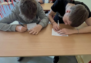 uczniowie wypisujący pocztówki